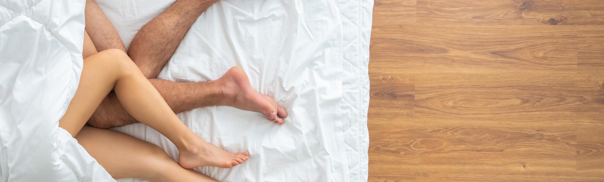 An aerial view of a bed, the intertwined legs of a man and a woman sticking out under the rumpled covers.