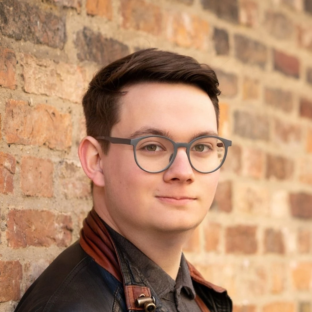 A headshot of Alex Keen, a white man in a leather jacket and glasses